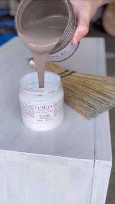 a person pouring paint on top of a white box with a broom and brush next to it