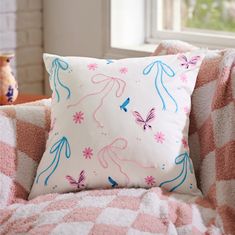 a pink and blue pillow sitting on top of a white couch next to a window