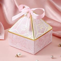 a pink and gold gift box with a bow on the top, surrounded by pearls