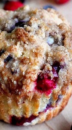 a close up of a muffin with crumbs on the top and blueberries in the background