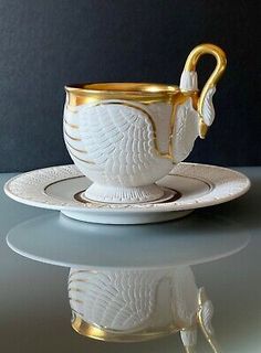 a white and gold coffee cup sitting on top of a saucer next to a spoon