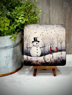 a painting of a snowman with a cardinal sitting on it's head next to a potted plant