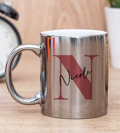 a silver coffee mug with the word nice on it next to an alarm clock and potted plant