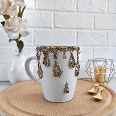 a white coffee cup with gold drops on it sitting on a wooden tray next to a vase