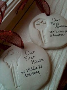 two white ceramic ornaments with red ribbon and name written on the front one is for our first house