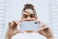 a man with dreadlocks taking a selfie in front of a white brick wall