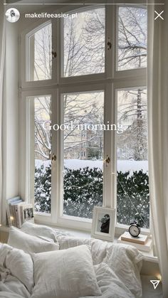 a bed with white sheets and pillows in front of a window that has snow outside