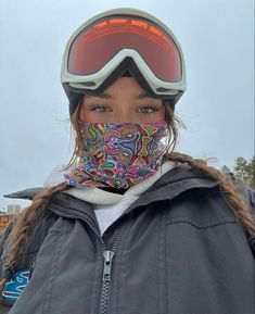 a woman wearing ski goggles and a colorful scarf on her face is standing in front of the camera