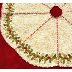 a quilted table topper with holly leaves and berries on the edge, sitting on a red surface