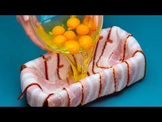 a person pouring orange juice into a bowl with bacon and eggs in it on a blue surface