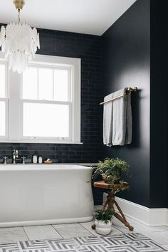 a white bath tub sitting under a window next to a wooden table and potted plant