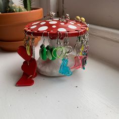 a red mushroom with earrings hanging from it's sides on a table next to a potted plant