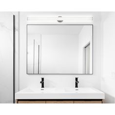 a white bathroom with two sinks and a large mirror above the sink is an illuminated light