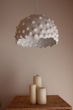 three candles sitting on top of a wooden table next to a white light fixture hanging from the ceiling