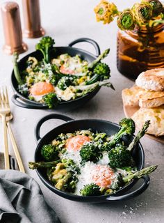 two black bowls filled with broccoli and other food on top of a table