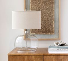 a glass lamp sitting on top of a wooden table next to a book and a painting