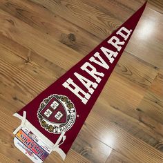 a maroon pennant with harvard seal on it sitting on a wooden floor next to some stickers