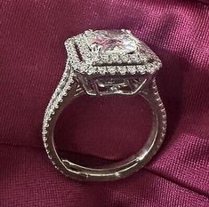 an engagement ring with a princess cut diamond surrounded by pave diamonds on a purple cloth