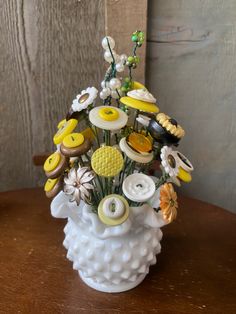 a white vase filled with lots of different types of buttons on top of a wooden table