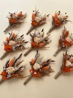 six dried flowers and feathers arranged on a table top with oranges, browns and white colors