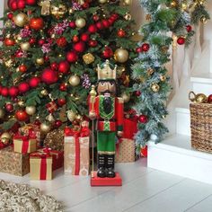 a christmas tree with presents under it and a nutcracker statue next to it