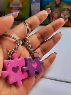 two pieces of pink and purple puzzle piece keychain being held by someone's hand