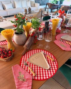 the table is set with red and white checkered placemats, wine glasses, cheese wedges, pasta