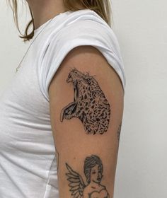 a woman with a leopard and angel tattoo on her arm, next to a white wall