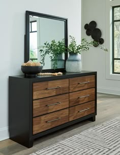 a black and brown dresser with a mirror on it's top, next to a potted plant