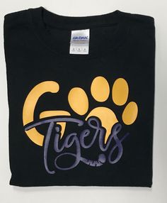 Go Tigers vinyl shirt. Mascot name can be changed to fit your needs. Shirt style may vary depending on availability. Available in adult sizes upon request. Vinyl can be done in a different color. Please leave me a note for any color changes. Made in a smoke free and pet free home. Thank you for visiting my shop! Have a blessed day! Black T-shirt With Heat Transfer Vinyl For School, Black Screen Print T-shirt For School, Black T-shirt With Screen Print For School, Black Text Print Shirt For School, Black Cotton Screen Print Transfers, Black Letter Print Shirt For Game Day, Black Shirt With Letter Print For Game Day, Black Custom Print T-shirt For College, Black Cotton School Spirit Shirt