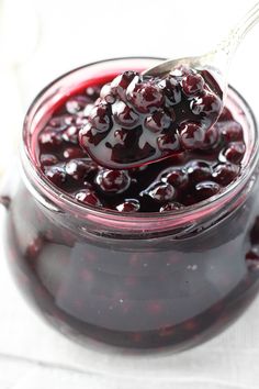 a spoon full of blueberry jam on top of a white tablecloth with berries in the jar