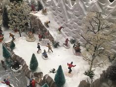 a toy town with snow covered trees and people on sleds in the snow