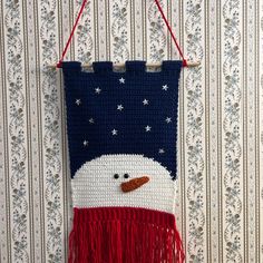 a crocheted snowman hanging on a wall next to a striped wallpaper