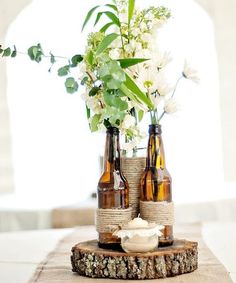 two beer bottles with flowers in them sitting on a piece of burlocked wood