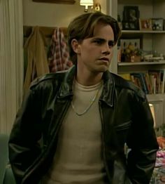 the young man is wearing a leather jacket and standing in front of a book shelf