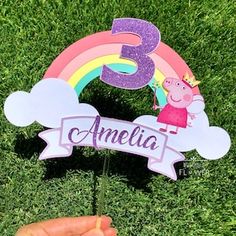 a hand holding up a cake topper with the number three in front of it