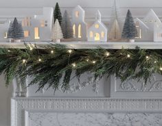 a fireplace mantel decorated with christmas trees and lit up houses on top of it