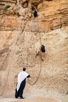 two men climbing up the side of a cliff with rope attached to it's sides