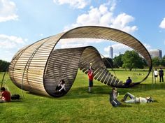 people sitting on the grass in front of a large wooden structure that looks like a boat