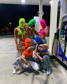 five people in neon colored masks at a gas station