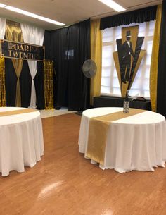 two round tables with white tablecloths on them in front of black and gold drapes