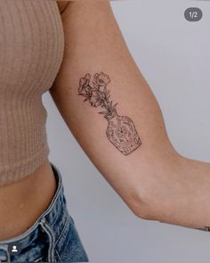 a woman's arm with a tattoo on it and flowers in a vase behind the arm