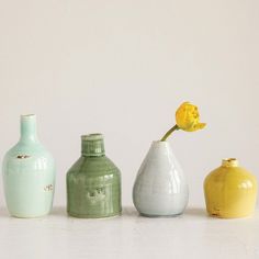 three vases with one yellow flower in the middle and two green ones behind them