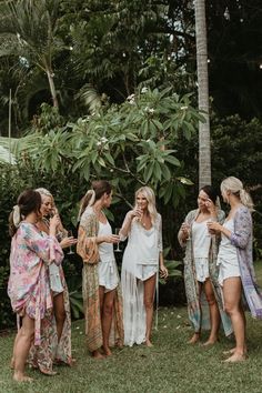 four women in white robes standing around each other and talking to one another while the others are holding their hair combs