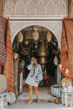 a woman standing in front of a store with lots of hanging lamps and pots on the wall