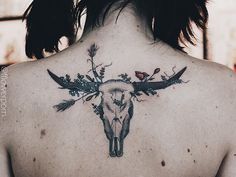 the back of a woman's neck with an animal skull and flowers on it