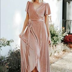 a woman wearing a pink dress and sandals standing in front of a white wall with flowers