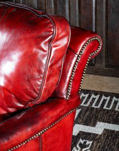 a red leather chair with studded arms and foot rests on a rug in front of a wooden wall