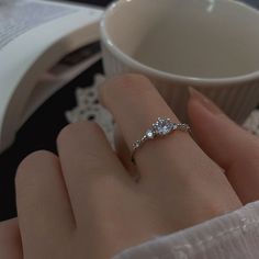 a woman's hand with a diamond ring on her finger next to a coffee cup