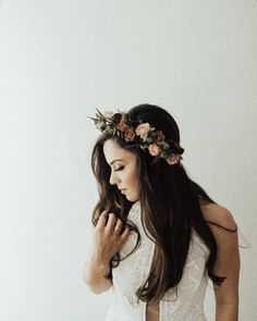 a woman with long hair wearing a flower crown and holding her hand to her face